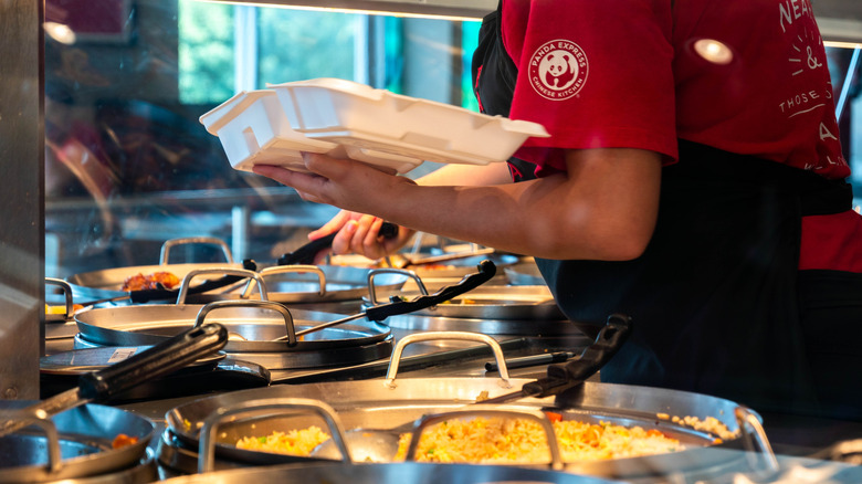 Employee spooning Panda Express food into a styrofoam box.