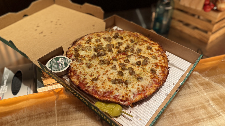 a sausage and pepperoni Pan Pizza by Papa Johns in a box with banana pepper on side and packet of garlic sauce