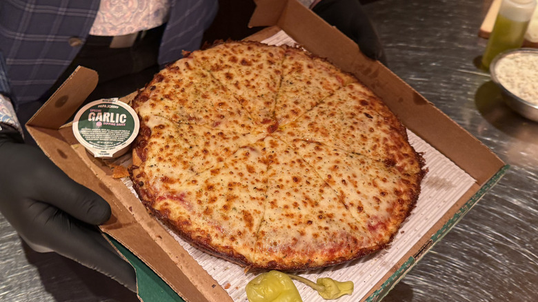 a plain cheese Papa Johns Pan Pizza in takeout box next to banana pepper and takeout sauce packet of garlic
