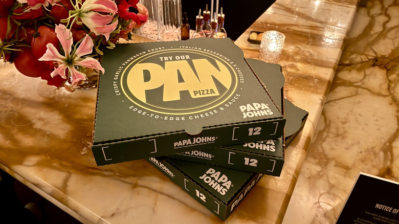 Papa Johns Pan Pizza boxes stacked on marble bar counter next to bouquet of flowers
