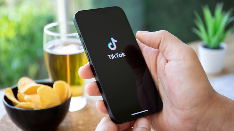 A hand holding a phone with the TikTok app open.