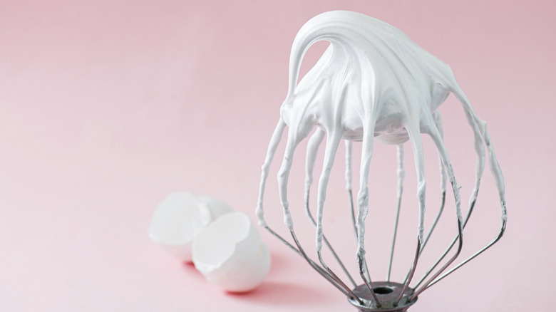 A whisk topped with marshmallow fluff on a pink background.