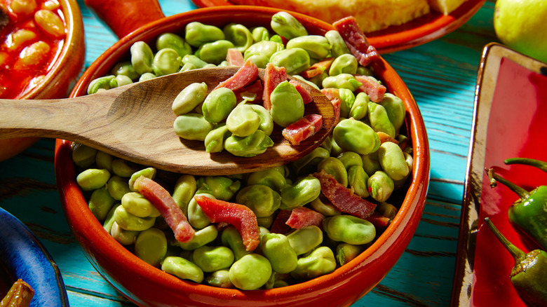Lima beans with ham in a bowl, being mixed with a wooden spoon