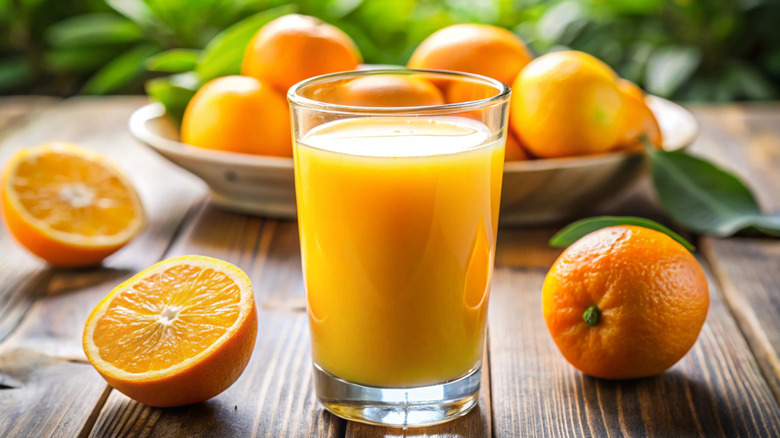 A glass of orange juice and halved oranges