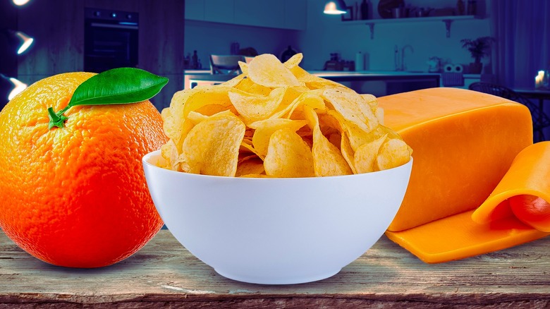 An orange, potato chips, and cheese on a wooden plank