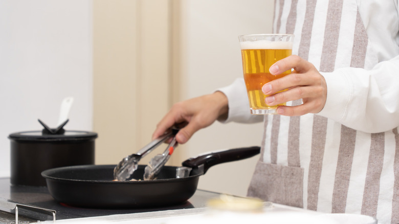 a person cooks while holding a glass of beer