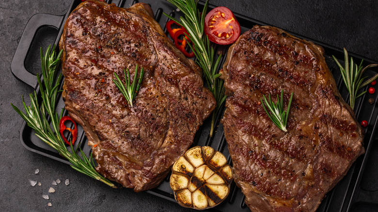 Two large, grilled and heavily seasoned steaks with grilled pineapple, tomato, and rosmeary