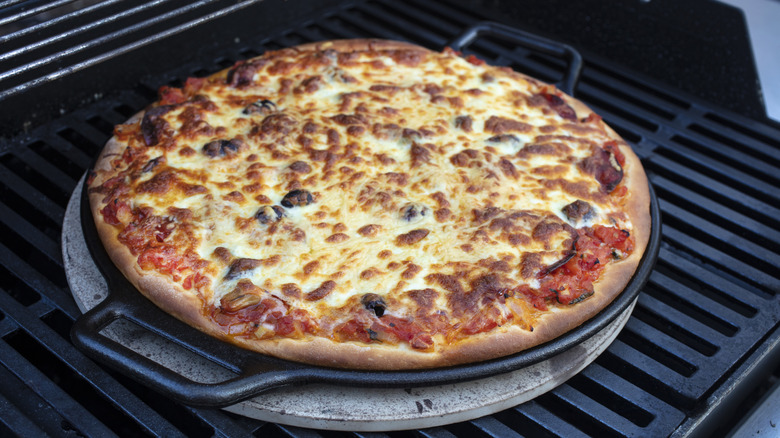 A nearly-done pizza cooking on a grill