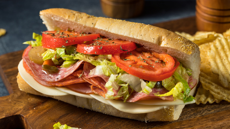 An Italian-style hoagie on a wooden plank with potato chips