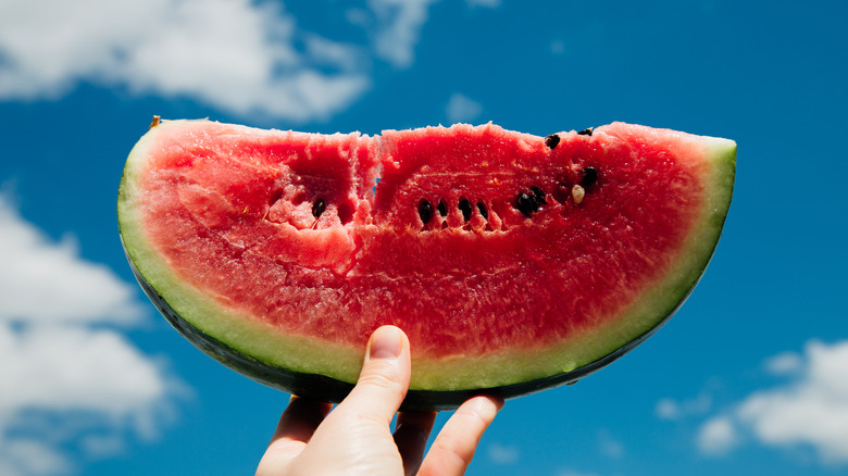 Hand holding up a wedge of watermelon against blue sky