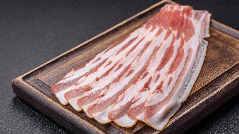 Fresh, raw bacon slices on a wooden cutting board