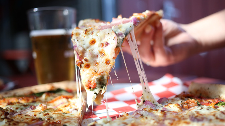 A close up of a cheese-pull of a pizza in front of a glass of beer