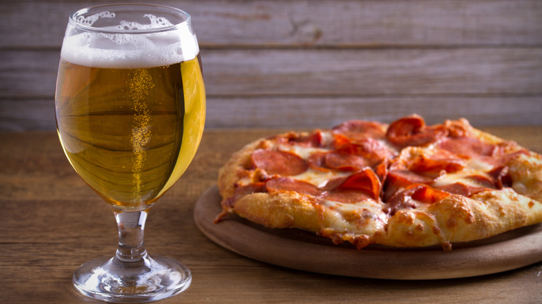 A glass of light beer next to a pepperoni pizza