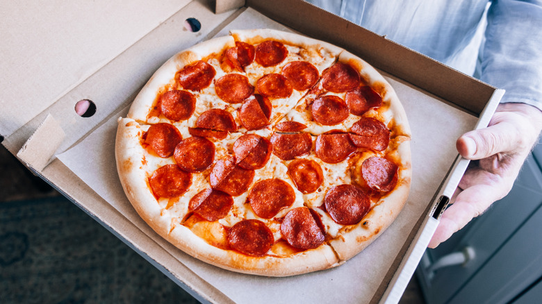 A person holds a pepperoni pizza in an open cardboard box