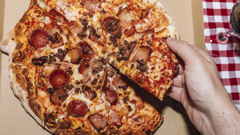 Person takes slice of pepperoni from a pizza on a cardboard box