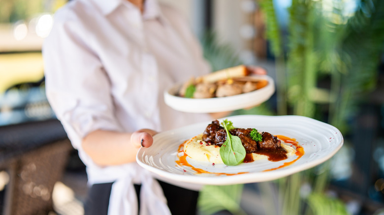Restaurant server bringing plate of beef tips with mashed potatoes to table