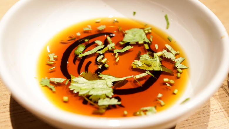 a small dish of homemade ponzu sauce with cilantro leaves and chives floating in it