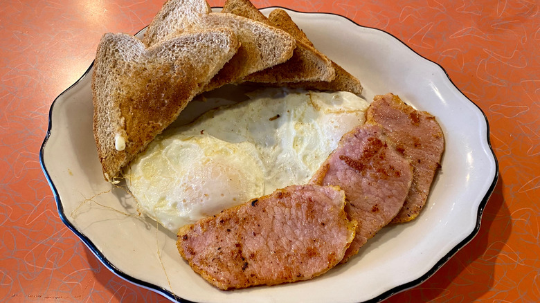 Peameal bacon slices with eggs and toast on a white plate