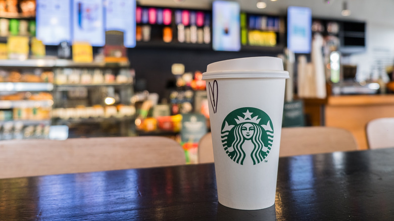 A Starbucks coffee cup with a heart on it on a table inside of a Starbucks location.