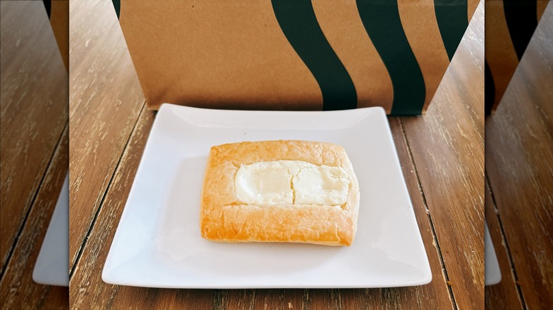 Starbucks cheese danish on a white plate with Starbucks bag in the background