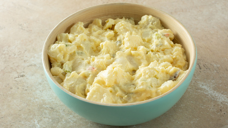 Potato salad in a white bowl garnished with sliced green onions