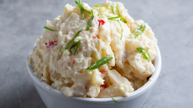 Potato salad in a white bowl garnished with sliced green onions.