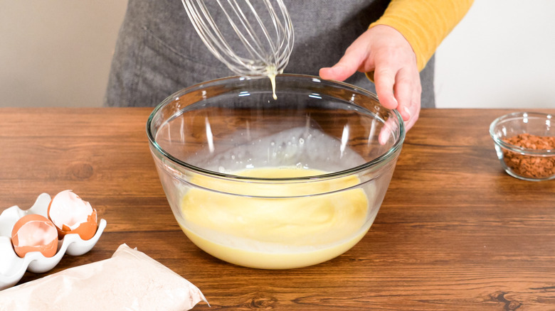 person using a whisk to combine pound cake ingredients in glass bowl
