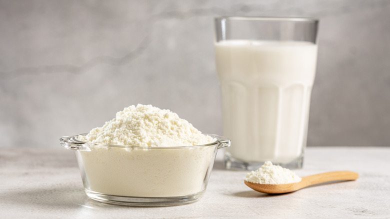 A glass bowl of powdered milk beside a glass cup of milk