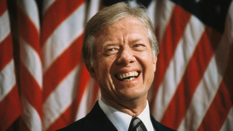 Former President Jimmy Carter smiling in front of an American flag