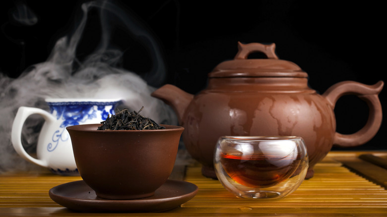 A brown teapot and cups with tea leaves and brewed tea