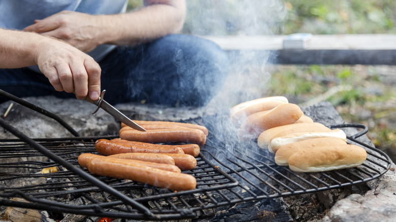 A person slicing open hot dogs as they cook on the grill