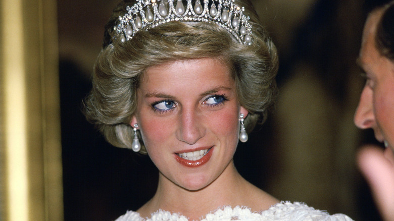 Princess Diana wearing a crown and earrings smiling as she speaks to her husband.