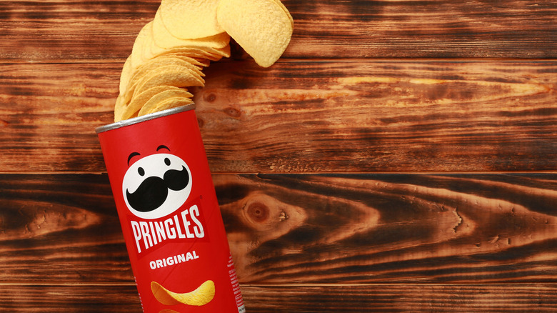 Top view of an open tube of Pringles laying on its side alongside Pringles chips on a wooden table