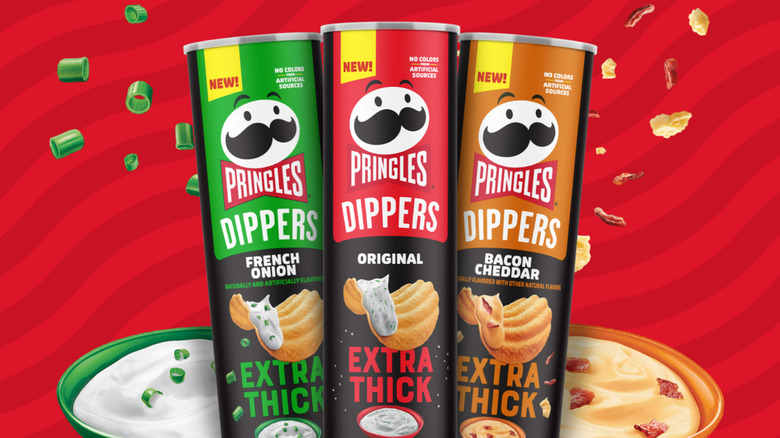 Three cans of Pringles Dippers on a red striped background with a bowl of white dip and a bowl of yellow dip behind them