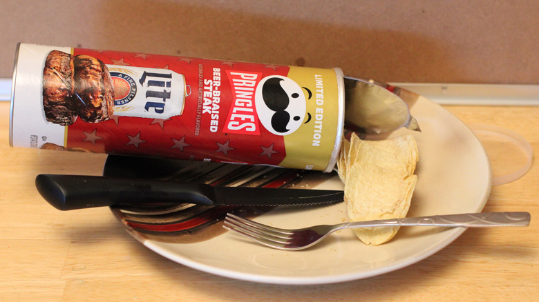 A can of the Pringles x Miller Lite beer-braised steak flavored chips on a plate with a fork and knife