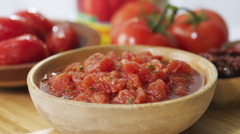 Canned diced tomato in a bowl with fresh tomatoes in the background