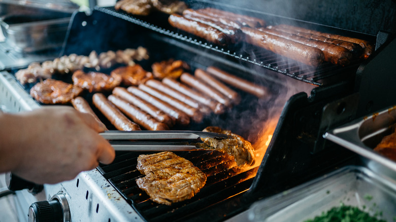 A loaded gas grill with various types of meats cooking