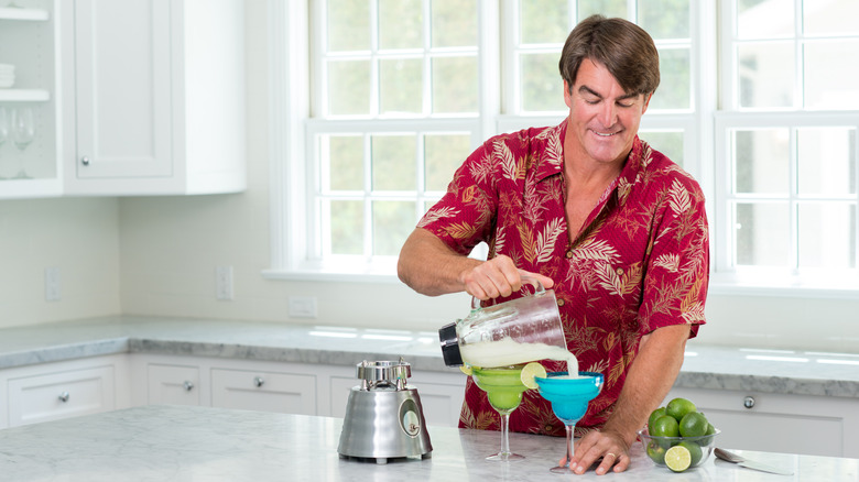 A man pours frozen margaritas from a blender in a white kitchen