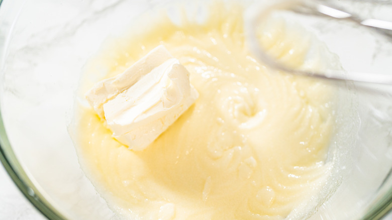Cream cheese block added to butter and sugar mixture for cookies in clear bowl