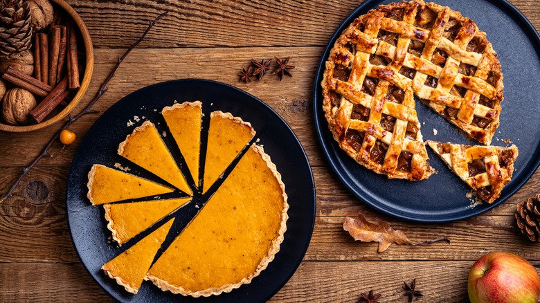 Pumpkin pie and apple pie with seasonings on a wood table