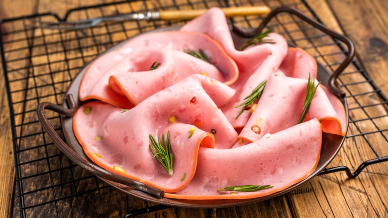 Sliced mortadella with sprigs of rosemary on dark plate