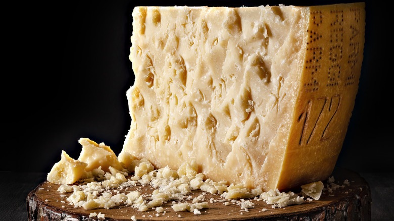 An aged Parmigiano-Reggiano wheel on a cutting board with chunks and crumbles around it.