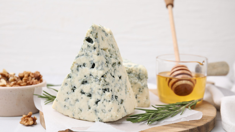 Blue cheese on a plate next to a bowl of walnuts and a small pitcher of honey.