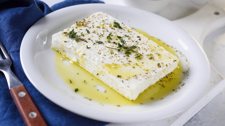A block of feta cheese on a plate, drizzled with olive oil, and garnished with herbs.