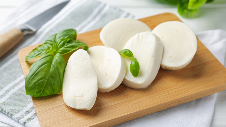 Slices of fresh mozzarella cheese on a cutting board with fresh basil leaves.