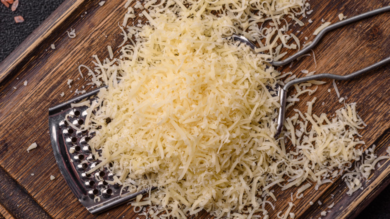 A pile of grated Parmesan cheese on top of a grater on a cutting board.