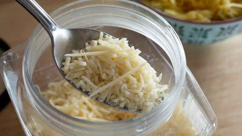 A spoon taking pre-shredded cheese out of a jar.