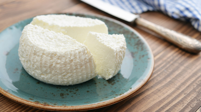 Fresh ricotta cheese on a plate on a wooden table with a knife in the background.