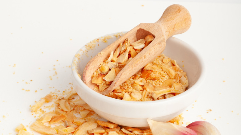 dried garlic chips in bowl and outside of bowl with wooden scooper resting on top of chips