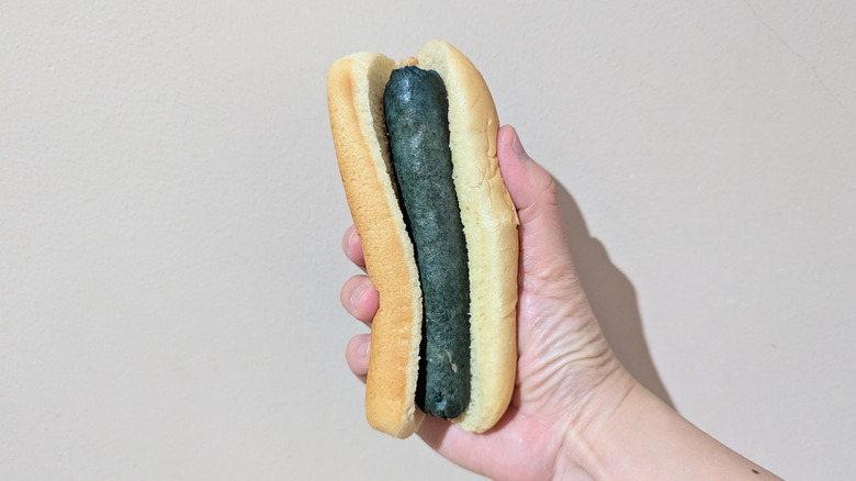 Hand holding blue hot dog in a bun.